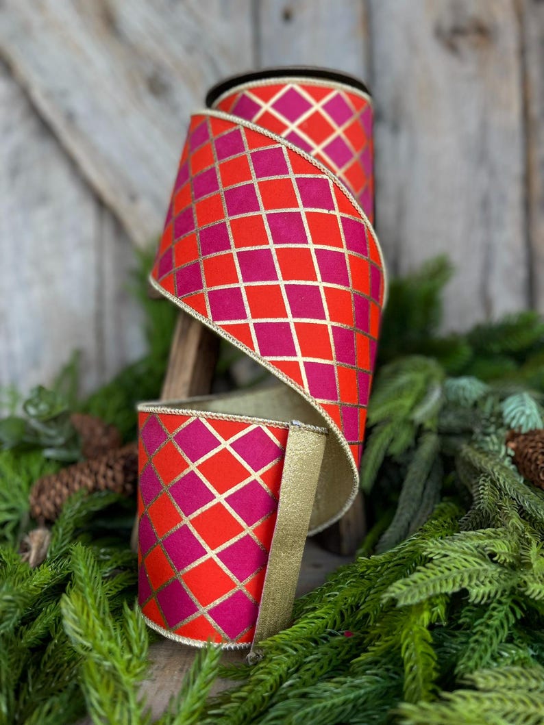 May include: A roll of decorative ribbon with a vibrant geometric pattern. The ribbon features a repeating diamond grid design in shades of red and fuchsia, accented with gold lines. The edges are trimmed with gold. Perfect for crafting and holiday decor.