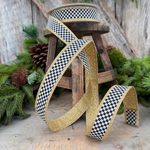 May include: A spool of decorative ribbon featuring a black and white checkered pattern on one side and a solid gold glitter finish on the other. The ribbon is draped in loops, showcasing the contrasting textures and colors of the fabric material.