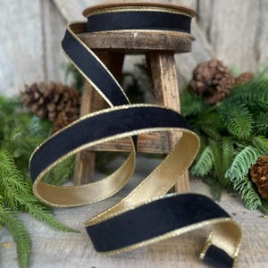 May include: Black velvet ribbon with a gold trim. The ribbon is rolled up on a wooden stool and is surrounded by pine branches.