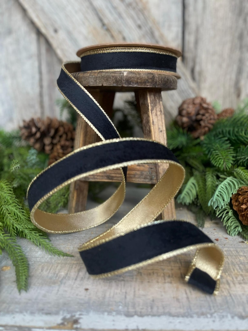 May include: Black velvet ribbon with a gold trim. The ribbon is rolled up on a wooden stool and is surrounded by pine branches.