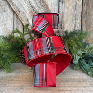 May include: A roll of wired ribbon featuring a red, grey, and black plaid pattern with thin metallic gold and green accent stripes. The fabric ribbon is displayed in a cascading loop, showing the vibrant red interior and the detailed tartan design.