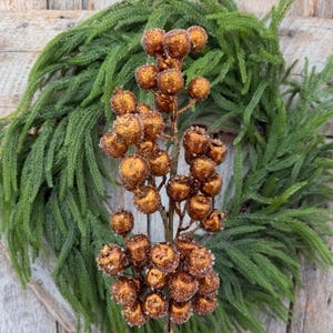 May include: A decorative floral pick featuring numerous round, copper-colored berries with a textured, glittery finish. The berries are clustered along a central brown stem, creating a dense, spherical arrangement that mimics natural fruit.