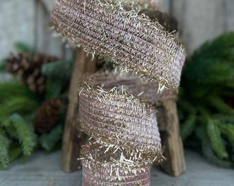 May include: A spool of pink and gold wired ribbon with a frayed edge. The ribbon is wrapped around a wooden spool.