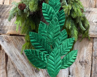 May include: A decorative artificial stem featuring multiple pointed, vibrant green leaves with a textured, glittery finish. The leaves are arranged in a layered, symmetrical pattern on a central stalk, creating a dense, foliage-like appearance.