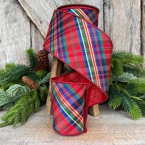 May include: A roll of wired ribbon featuring a classic plaid pattern in red, green, blue, and gold. The fabric has a smooth texture with a distinct tartan design, showcasing intersecting lines and a vibrant color palette suitable for holiday decor.