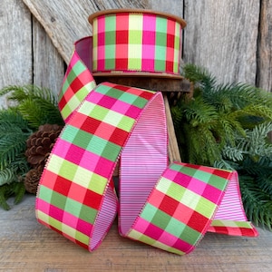 May include: A spool of colorful ribbon with a vibrant plaid pattern in shades of pink, red, green, and yellow. The ribbon is displayed with a portion unrolled, revealing a striped underside. The ribbon is perfect for crafting and gift wrapping.