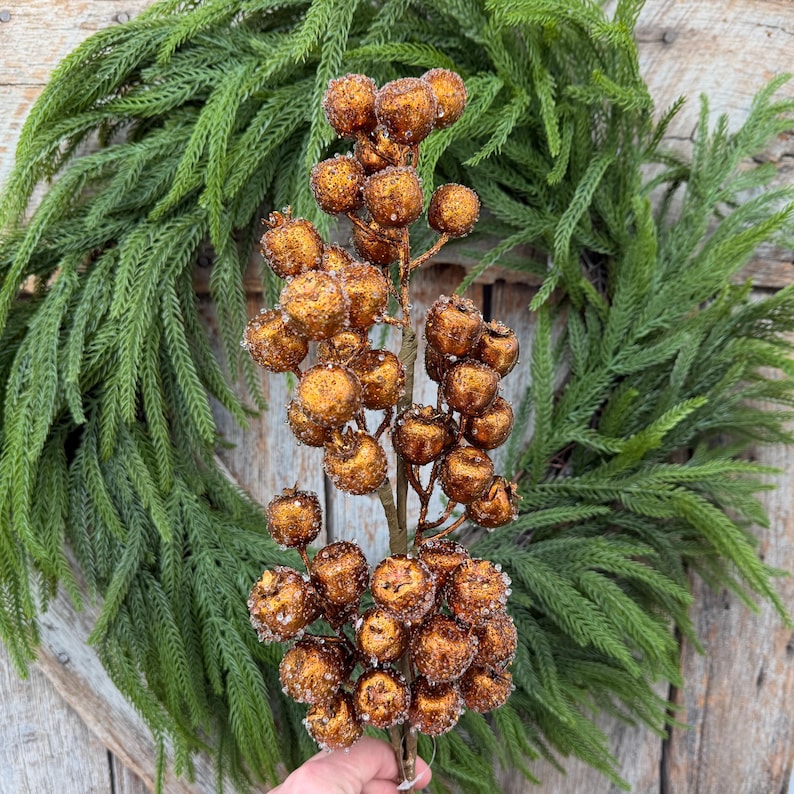 May include: A decorative branch featuring numerous round, metallic copper-colored berries with a textured, glittery finish. The berries are clustered along thin, brown stems, creating a dense, spherical arrangement that mimics a natural fruit spray.