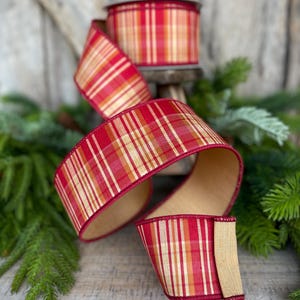 May include: A roll of red and gold plaid ribbon with a wired edge. The ribbon is displayed with a portion unrolled, revealing a natural-colored underside. The ribbon is suitable for holiday and craft projects.