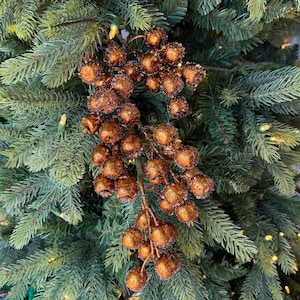 May include: A decorative branch featuring numerous round, copper-colored berries with a textured, glittery finish. The berries are clustered together on a central stem, creating a dense, spherical arrangement that hangs against green pine needles.