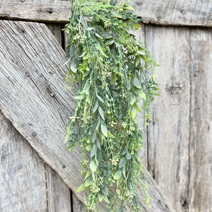May include: A long, green, artificial plant with small white flowers hanging from a wooden surface.