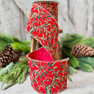 May include: A roll of red ribbon with a gold trim and a repeating pattern of black and green leaves. The ribbon is displayed with pine needles and pine cones, suggesting a holiday theme.