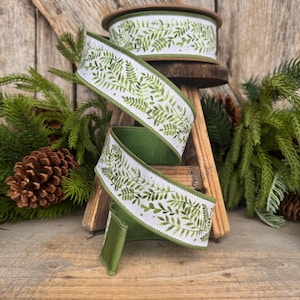 May include: A spool of wired ribbon featuring a white background with a repeating green fern leaf pattern. The ribbon has a solid green underside and finished edges. The design displays various shades of green foliage in a botanical style.