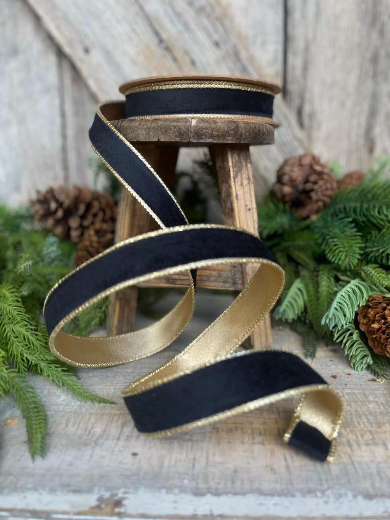 May include: Black velvet ribbon with gold trim. The ribbon is rolled up on a wooden stool and is surrounded by green pine branches.
