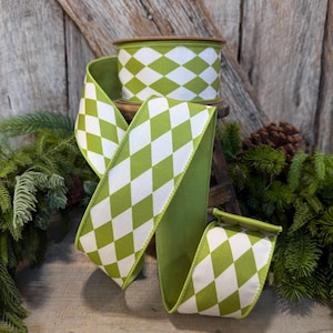 May include: A spool of wired ribbon featuring a repeating harlequin diamond pattern in lime green and white. The ribbon is wound into a cylindrical shape with loose ends cascading downward, showcasing the consistent geometric diamond design throughout.