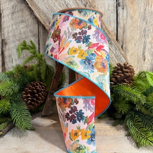 May include: A spool of wired ribbon featuring a watercolor floral pattern in shades of pink, orange, yellow, and blue. The ribbon has a bright turquoise stitched edge and a solid orange interior lining, coiled to display the vibrant botanical print.