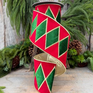 May include: A roll of wired ribbon featuring a vibrant red fabric base with a repeating pattern of dark green velvet diamonds outlined in gold metallic thread. The ribbon has a metallic gold interior lining and a structured, flexible edge.