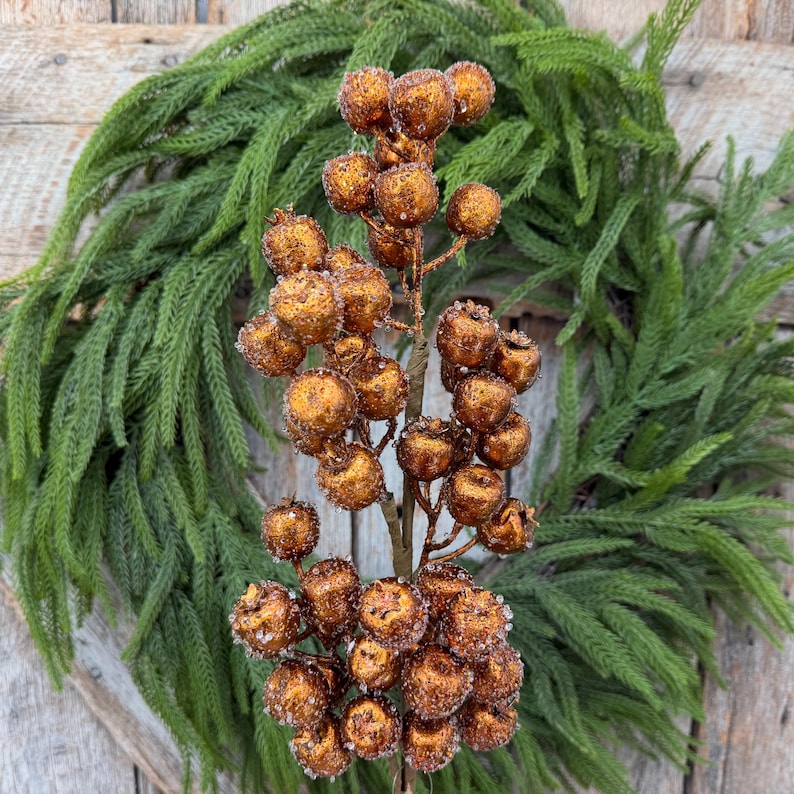 May include: A decorative floral pick featuring numerous round, copper-colored berries with a textured, glittery finish. The berries are clustered along a central brown stem, creating a dense, spherical arrangement that mimics natural fruit.
