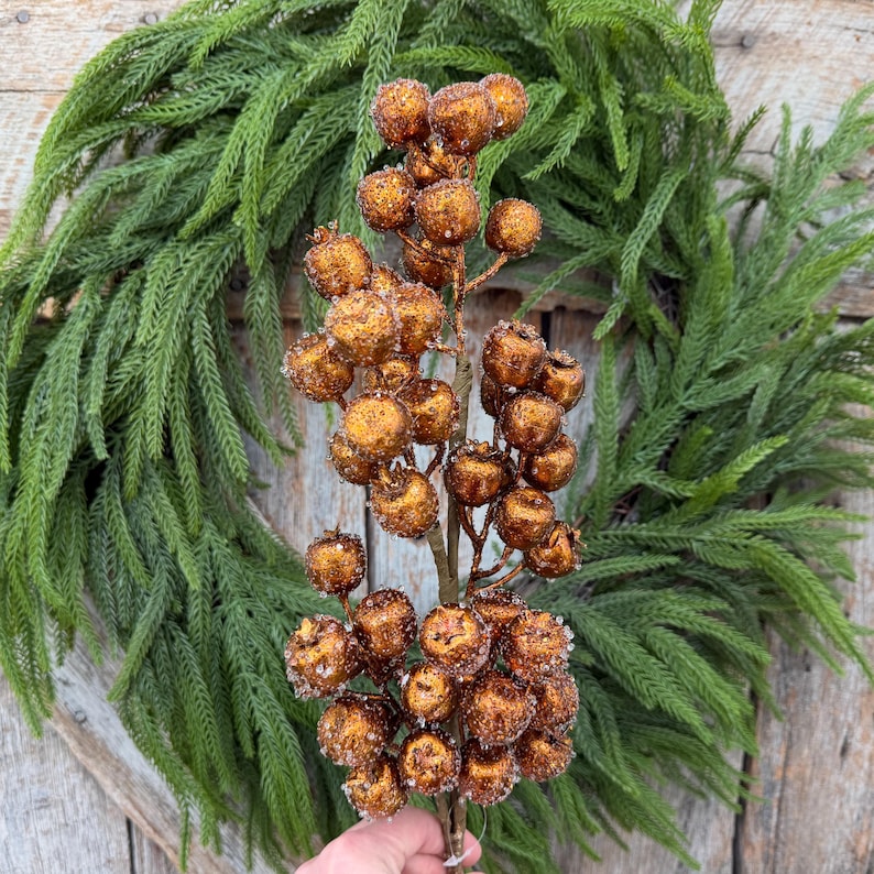 May include: A decorative floral stem featuring numerous round, copper-colored berries with a textured, glittery finish. The berries are clustered along thin, brown branches, creating a dense, spherical arrangement on a single vertical stem.