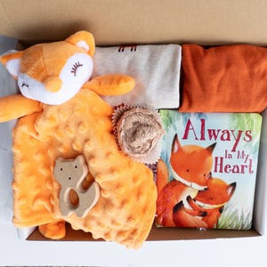 May include: A gift box filled with a plush orange fox toy, a textured orange blanket, a wooden fox-shaped teether, a light gray shirt, an orange shirt, and a children's book titled "Always In My Heart".