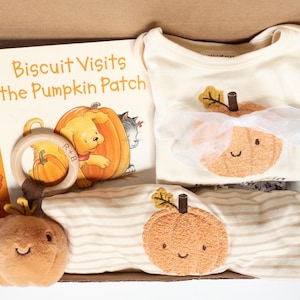May include: A gift box containing a children's book titled Biscuit Visits the Pumpkin Patch, a cream-colored bodysuit with a plush pumpkin appliqué and white ribbon, a striped long-sleeve shirt with a pumpkin patch, and a plush pumpkin toy.
