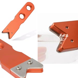 May include: Orange metal tool with two sharp points and a hole in the center. The tool is used to sharpen knives.