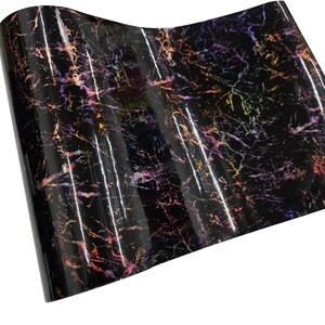 May include: A sheet of glossy black vinyl with a marble-like pattern. The design features streaks of orange, pink, purple, and yellow, creating a colorful, iridescent effect. The material is rolled and ready for use.