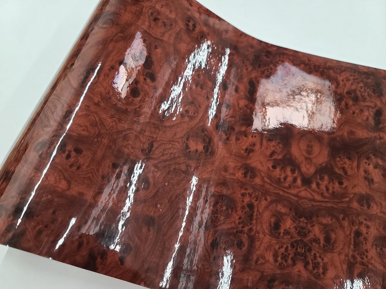 May include: A close-up of a brown woodgrain vinyl sheet with a glossy finish. The sheet has a realistic woodgrain pattern with dark brown and light brown tones.
