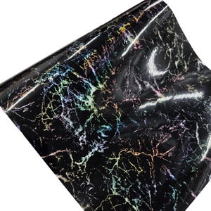 May include: A roll of black marble-patterned vinyl. The vinyl has a glossy finish with iridescent veining in shades of green, yellow, pink, and purple. The material is rolled up, showing the pattern and texture.