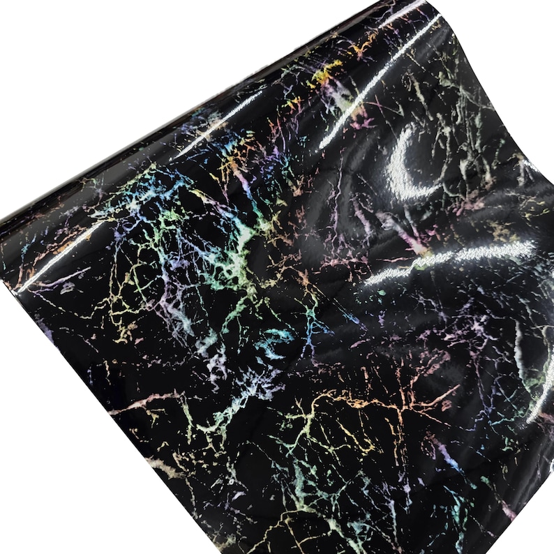 May include: A roll of black marble-patterned vinyl. The vinyl has a glossy finish with iridescent veining in shades of green, yellow, pink, and purple. The material is rolled up, showing the pattern and texture.