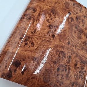 May include: A close-up of a brown woodgrain vinyl sheet with a glossy finish. The sheet has a realistic woodgrain pattern with dark brown knots and swirls.