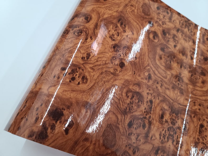 May include: A close-up of a brown woodgrain vinyl sheet with a glossy finish. The sheet has a realistic woodgrain pattern with dark brown knots and swirls.