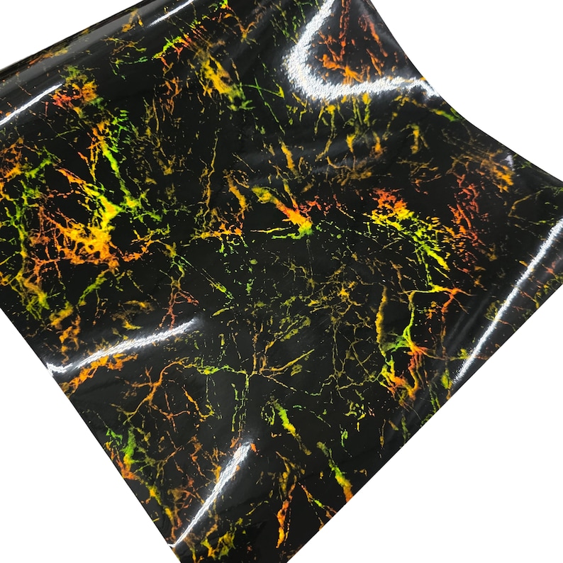 May include: A sheet of black vinyl with a glossy finish. The surface is patterned with a network of yellow, orange, and green veins, resembling a marble or stone texture. The material is folded and angled.