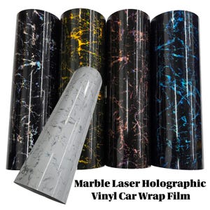 May include: Rolls of marble laser holographic vinyl car wrap film in various colors. The rolls include black, gold, purple, and blue marble patterns. A gray marble roll is in the foreground. The text "Marble Laser Holographic Vinyl Car Wrap Film" is at the bottom.