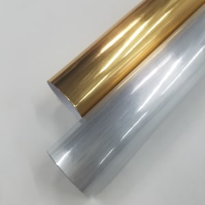 May include: Two rolls of adhesive vinyl, one gold and one silver, with a brushed metal finish. The rolls are partially unrolled and lying on a white surface.