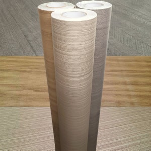 May include: Three rolls of wood-grain contact paper. The rolls are in different shades of brown and beige.