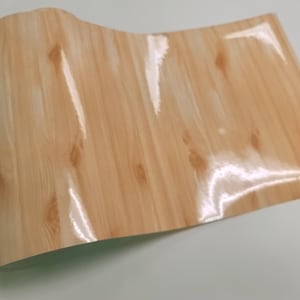May include: A sheet of wood-grain vinyl contact paper with a glossy finish. The paper has a light brown color with a wood grain pattern.