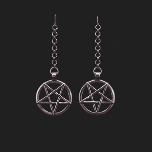 Pu&ograve; includere: Un paio di orecchini d'argento con un ciondolo a pentagramma su ogni orecchino. Gli orecchini sono su uno sfondo nero.