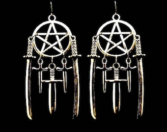 Puede incluir: Un par de pendientes de plata con un dije de pentagrama y espadas colgantes. Los pendientes son de estilo gótico.