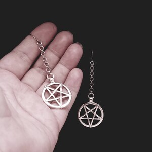 Pu&ograve; includere: Un paio di orecchini d'argento con un ciondolo a pentagramma su ogni orecchino. Gli orecchini sono appesi a una catena d'argento.