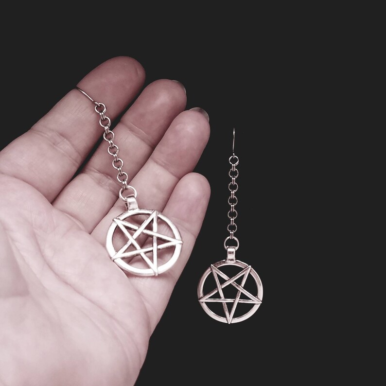 Pu&ograve; includere: Un paio di orecchini d'argento con un ciondolo a pentagramma su ogni orecchino. Gli orecchini sono appesi a una catena d'argento.
