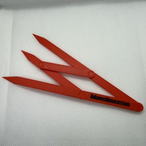 Puede incluir: Un compás de dibujo de plástico rojo con una inscripción negra que dice "AdamsDimension".