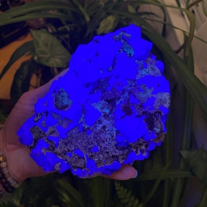 May include: A large, rough, blue-glowing rock with a dark gray, textured surface. The rock is being held in a hand.