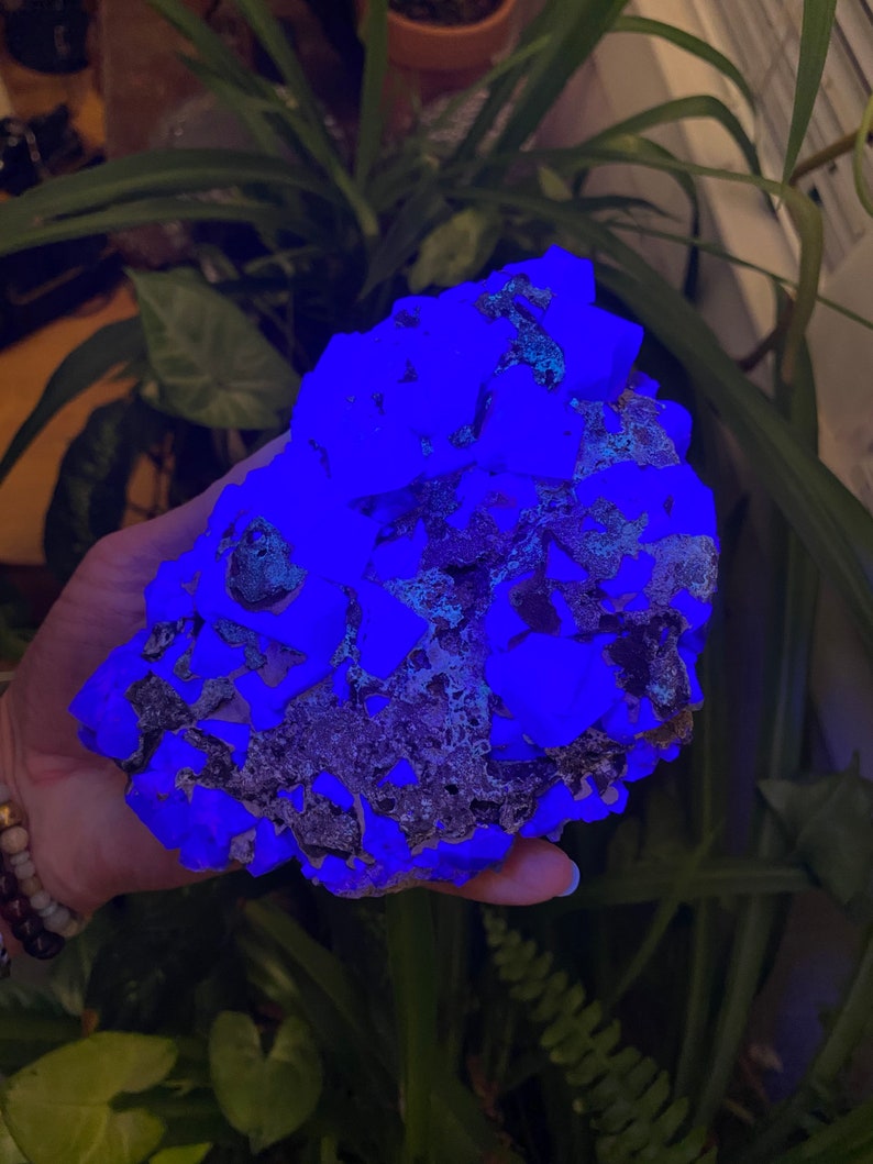 May include: A large, rough, blue-glowing rock with a dark gray, textured surface. The rock is being held in a hand.
