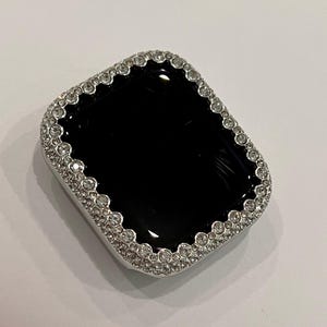 May include: A black Apple Watch face with a silver and clear crystal encrusted bezel.