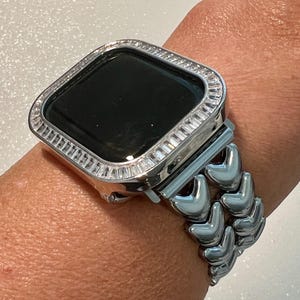 May include: A silver Apple Watch with a diamond-encrusted bezel and a silver chevron-style band.
