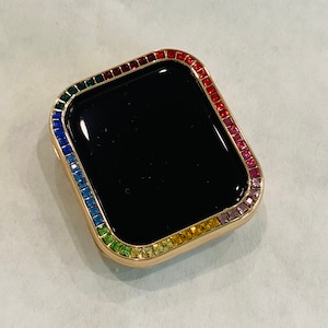 May include: A gold-coloured watch face cover with a rainbow-coloured crystal border.