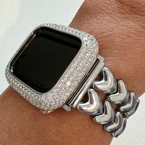 May include: A silver Apple Watch with a diamond-encrusted case and a silver heart-shaped link band.