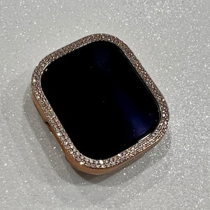 May include: A rose gold Apple Watch case with a clear, sparkly diamond-like bezel.