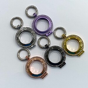 May include: Five silver, gold, and rose gold locket pendants with rhinestones. Each pendant has a round opening for a photo or other small item. The lockets are attached to silver, gold, and rose gold chains.