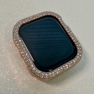 May include: A rose gold watch case with a clear crystal encrusted bezel. The case is designed to fit a smart watch.